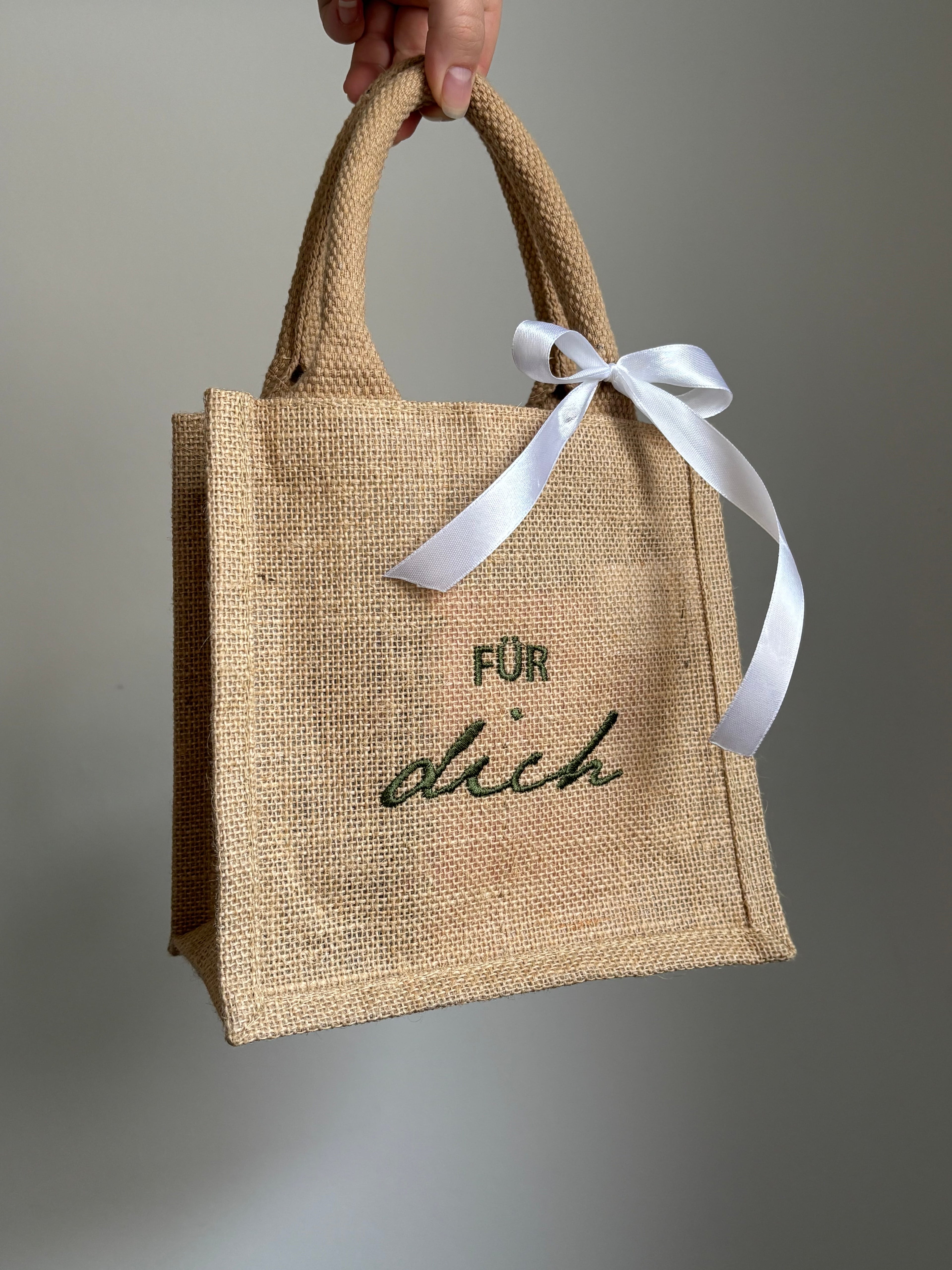 Eine bestickte Jute Petite Mini Bag mit einer weißen Schleife. Auf der Tasche ist der personalisierte Stick „Für dich“ in dunkelgrün gestickt.