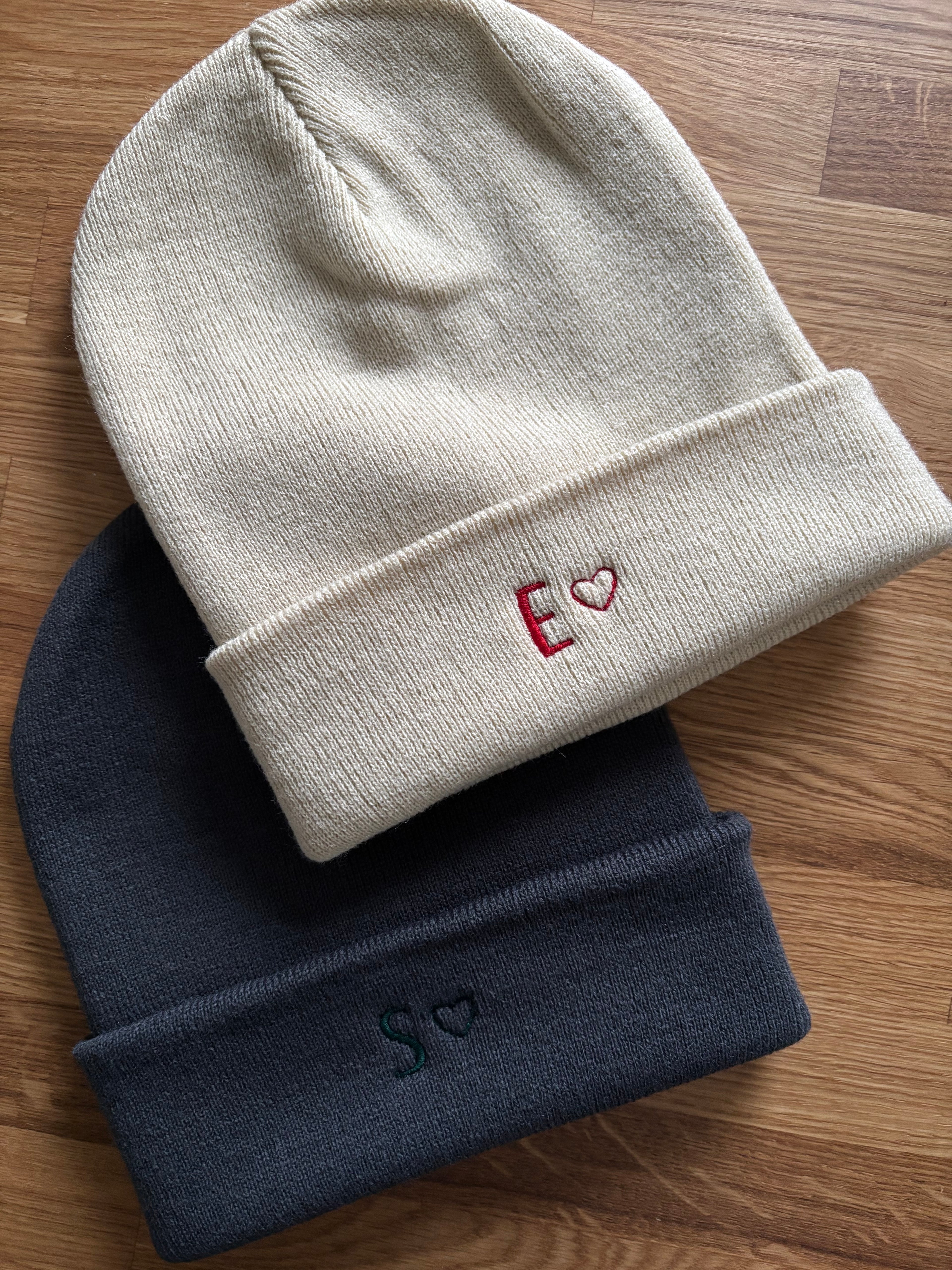 Zwei Mützen in almond und dunkegrau. Vorne ist jeweils ein Anfangsbuchstabe mit einem Herz gestickt.