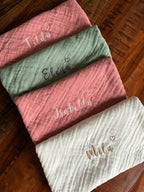 Es sind verschiedene Farben der Musselinstoff Spucktücher abgebildet. Auf jedem Tuch ist eine Namensstickerei, welche individuell und personalisiert abgestimmt ist. Zusätzlich zum Namen ist ein Herz gestickt.