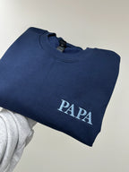 Ein Sweater in der Farbe Navy Blue. Der Stick ist in Stone Blue. Gestickt ist in Großbuchstaben Papa.