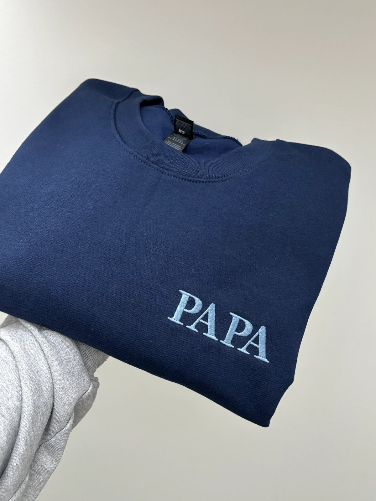 Ein Sweater in der Farbe Navy Blue. Der Stick ist in Stone Blue. Gestickt ist in Großbuchstaben Papa.