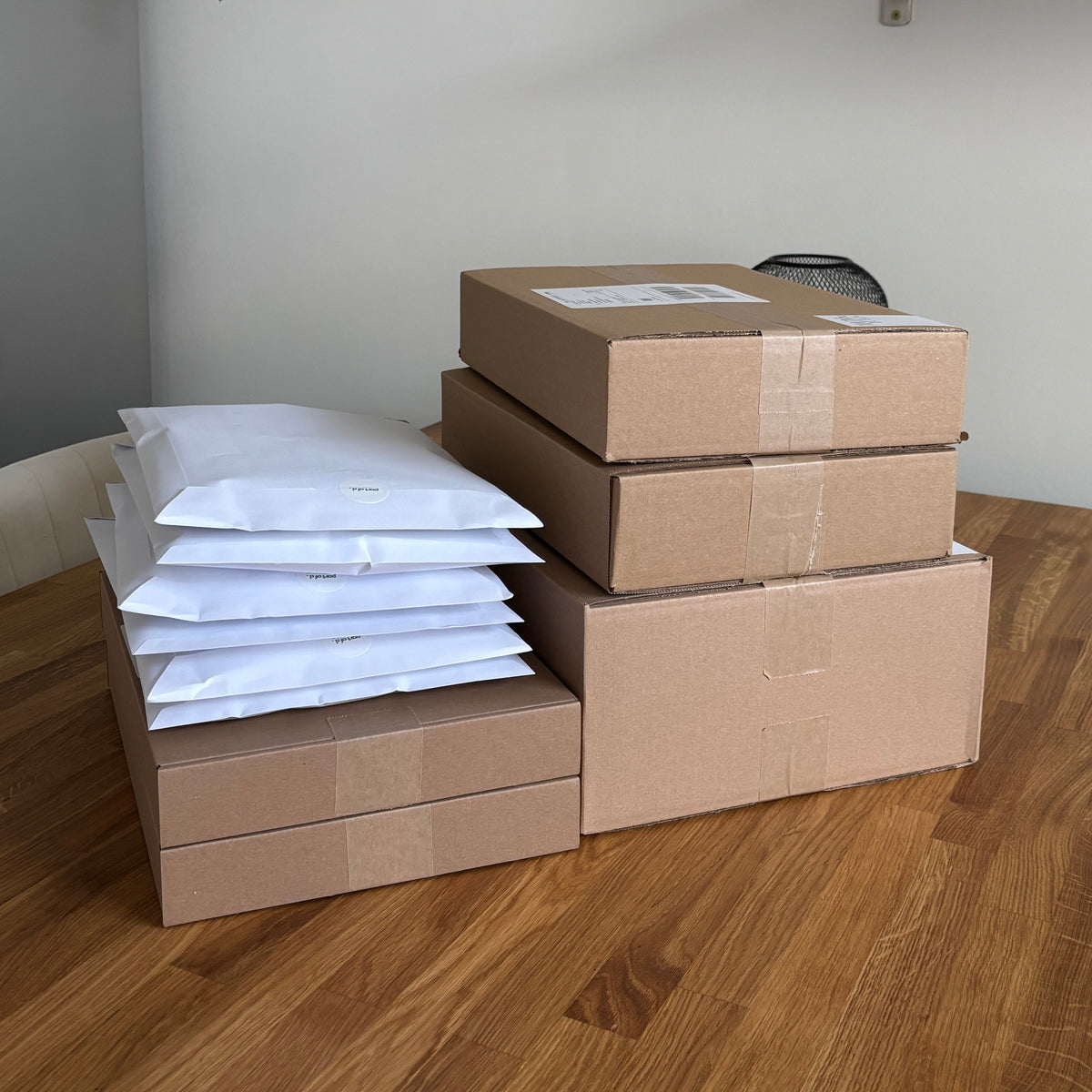 Verschieden große Pakete und Briefumschläge auf einem Holztisch. In den Paketen befinden sich Bestellungen von Kunden.