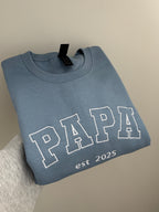 Ein bestickter Sweater in der Farbe Stone Blue PAPA est 2025 in der Garnfarbe weiß.