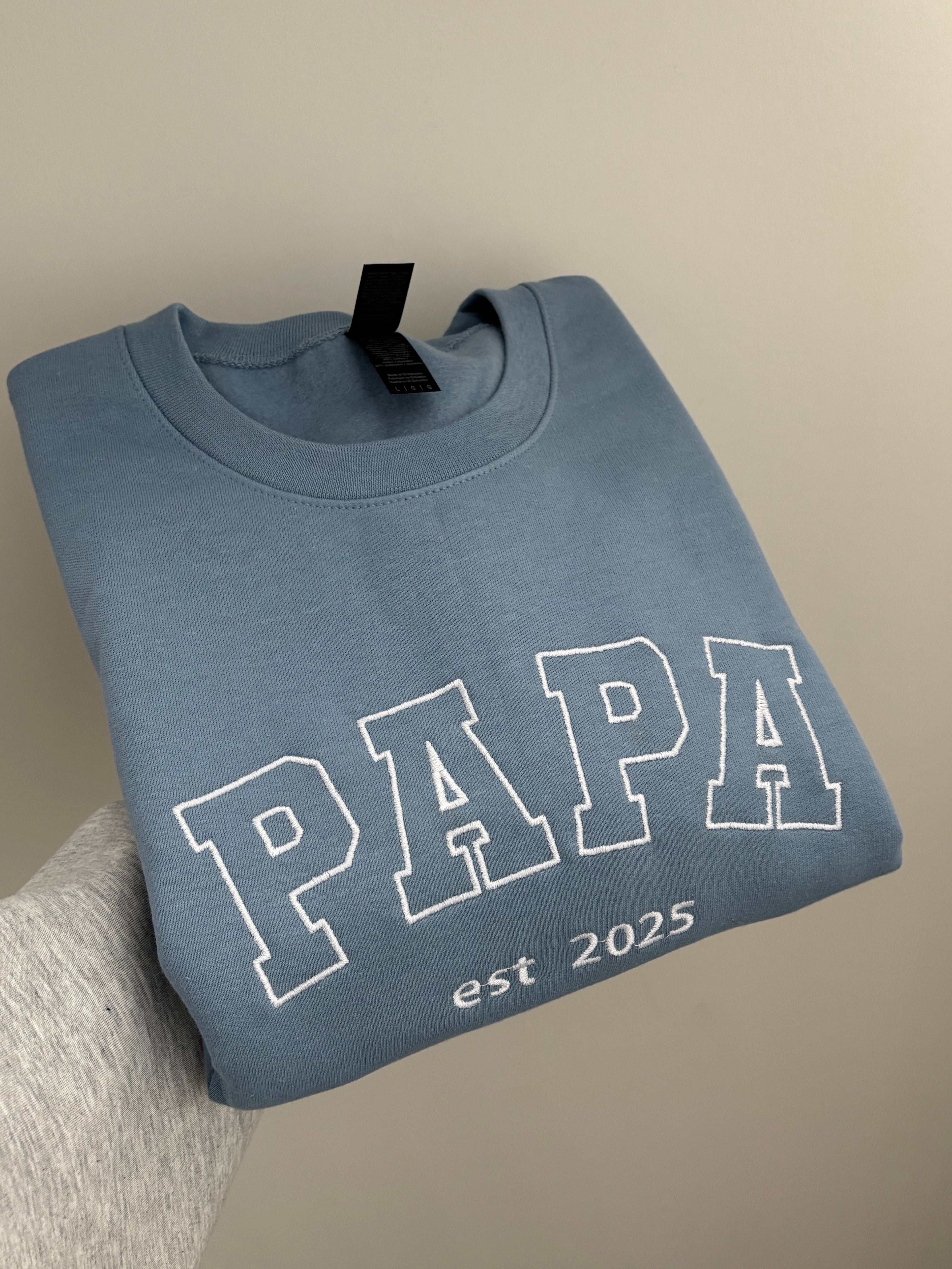 Ein bestickter Sweater in der Farbe Stone Blue PAPA est 2025 in der Garnfarbe weiß.