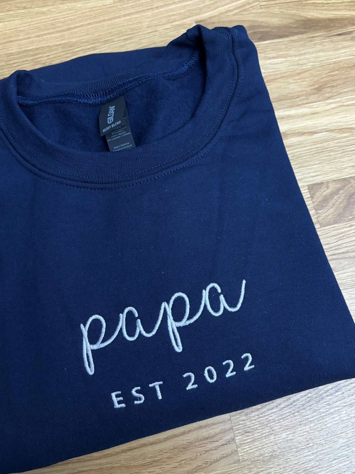 Ein Sweater in der Farbe Navy Blue mit einer Stickerei in weiß auf der Brust: Papa est 2022.
