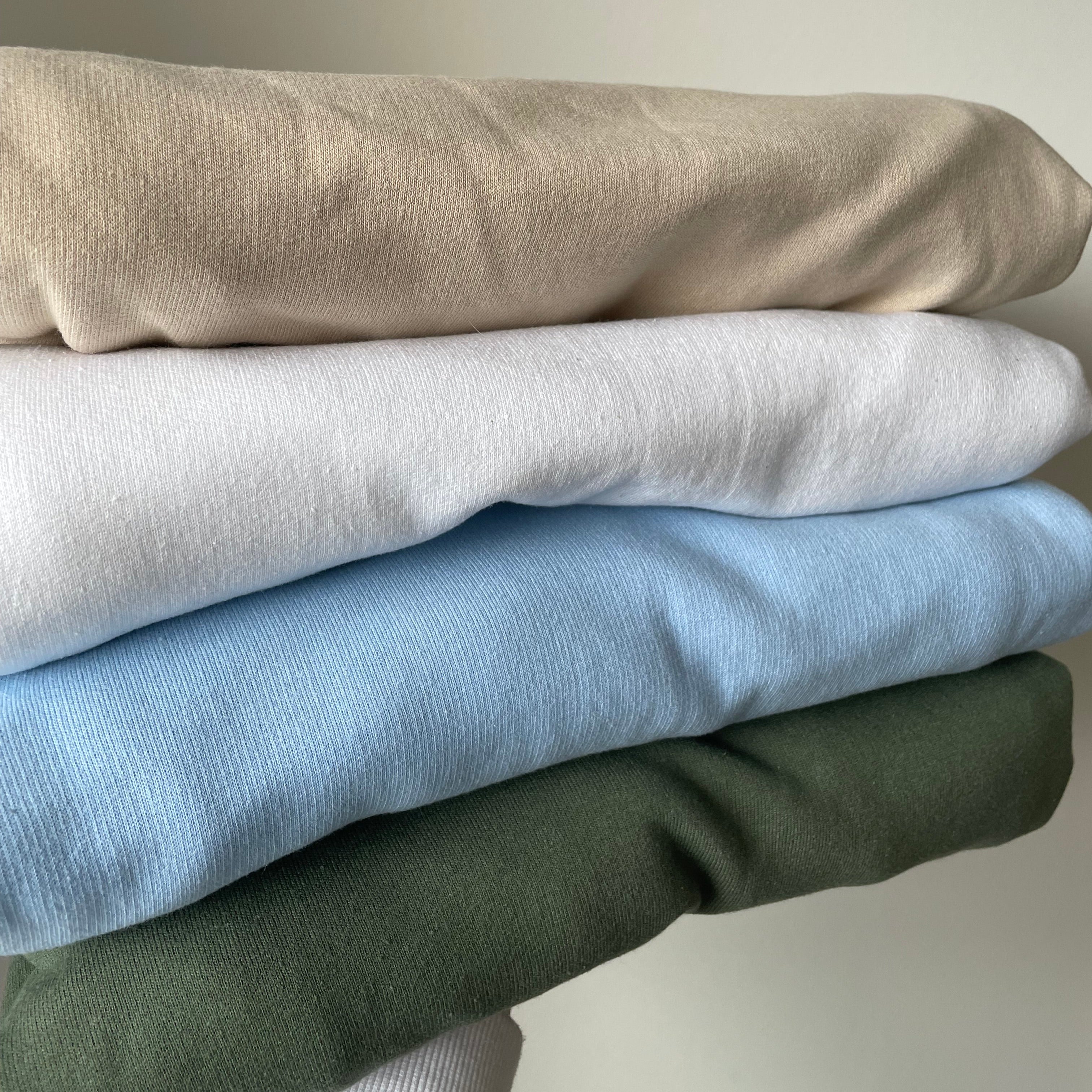 Auf einer Hand sind vier verschiedene Pullover. Die Farben sind beige, weiß, hellblau und military green. Die Sweater sind ordentlich gefaltet.