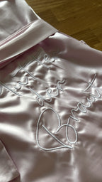 Ein rosa Satin Morgenmantel mit einer weißen Stickerei hinten auf dem Rücken: Mutter der Braut.