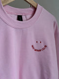 Ein Rosa Sweater ist mit einem roten Smiley auf der Brust bestickt: Hot Moms Club.