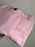 Ein Sweater in der Farbe Rosa mit einer Stickerei in der Farbe Rosa: Mama est. 2025.