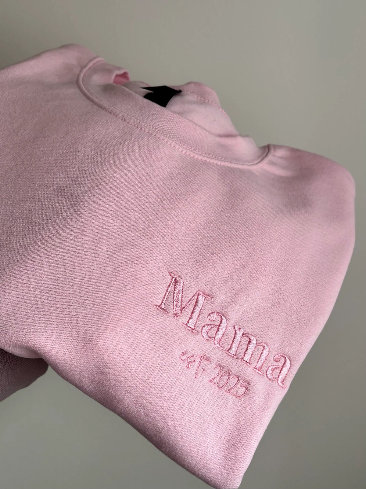 Ein Sweater in der Farbe Rosa mit einer Stickerei in der Farbe Rosa: Mama est. 2025.