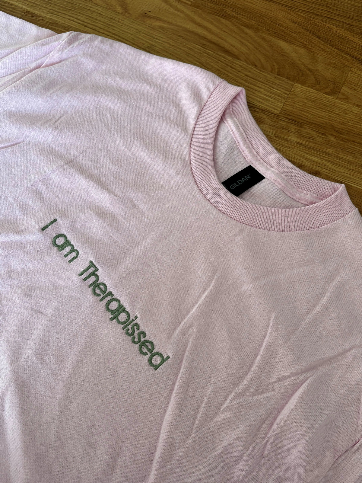Ein T-Shirt in der Farbe Rosa mit einer Stickerei in der Farbe Moss vorne mittig auf der Brust "I am Therapissed".
