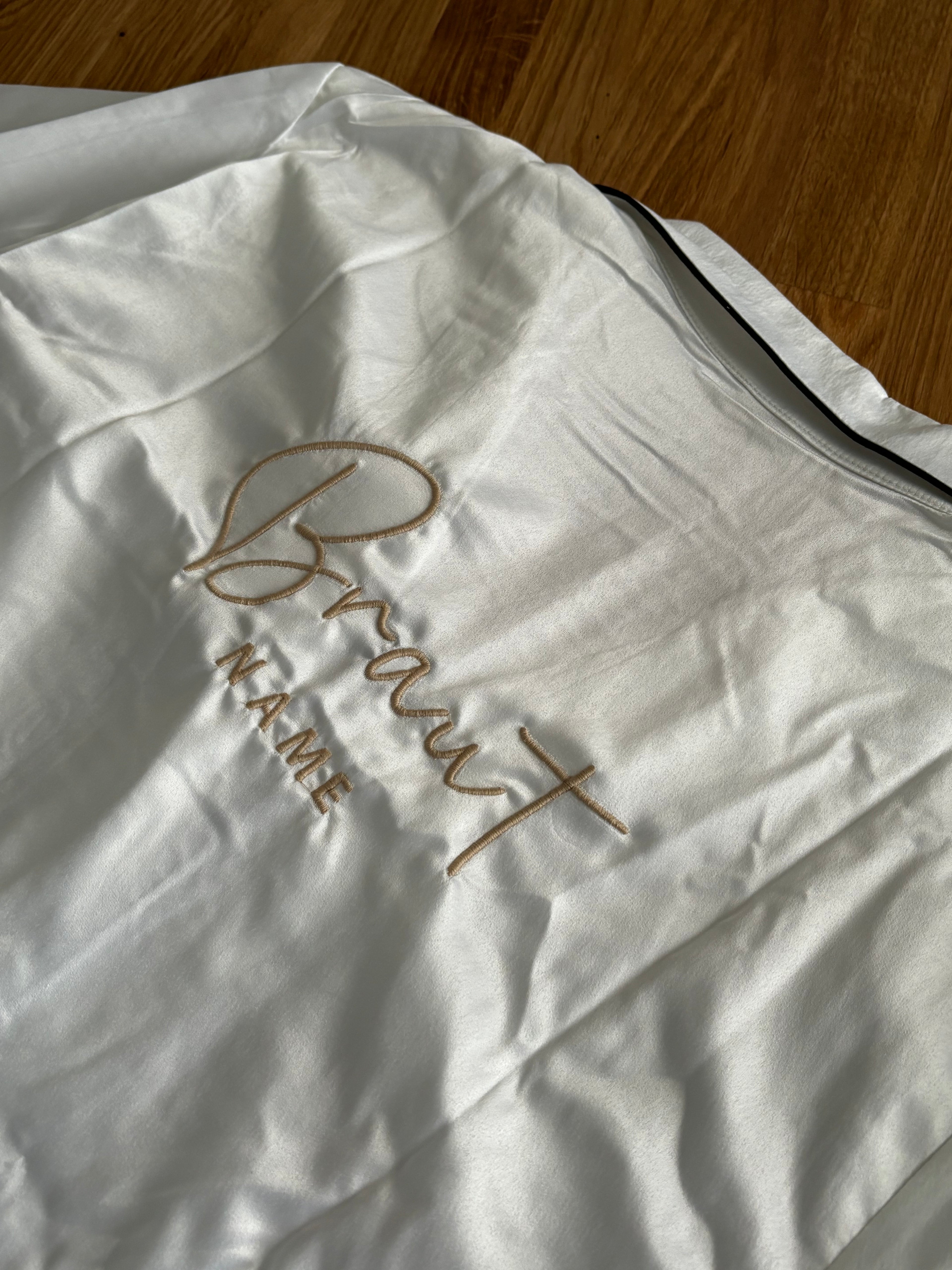 Ein weißes Pyjamaoberteil mit einem Stick auf dem Rücken. Der Stick ist Beige.