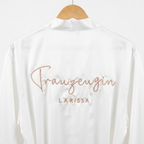 Ein weißer Satin-Morgenmantel mit einer personalisierten Stickerei hinten auf dem Rücken "Trauzeugin Larissa".