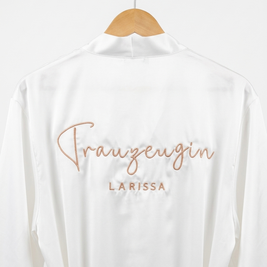 Ein weißer Satin-Morgenmantel mit einer personalisierten Stickerei hinten auf dem Rücken "Trauzeugin Larissa".