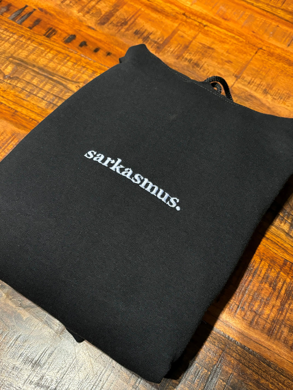 Ein schwarzer Hoodie mit einer Stickerei vorne auf der Brust: sarkasmus.