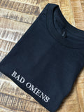 Ein T-Shirt in der Farbe Schwarz mit einer weißen Stickerei vorne mittig auf der Brust Bad Omens in Großbuchstaben.