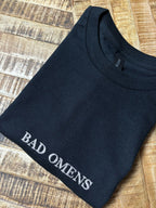 Ein T-Shirt in der Farbe Schwarz mit einer weißen Stickerei vorne mittig auf der Brust Bad Omens in Großbuchstaben.