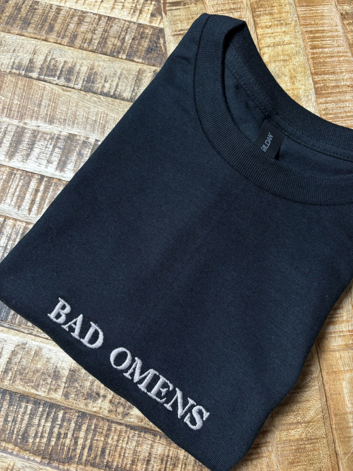 Ein T-Shirt in der Farbe Schwarz mit einer weißen Stickerei vorne mittig auf der Brust Bad Omens in Großbuchstaben.