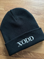 Eine schwarze Mütze mit einem weißen Stick "XODD".