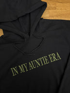Ein Hoodie in der Farbe Schwart mit dem Wunschtext „IN MY AUNTIE ERA“ in der Garnfarbe Green.