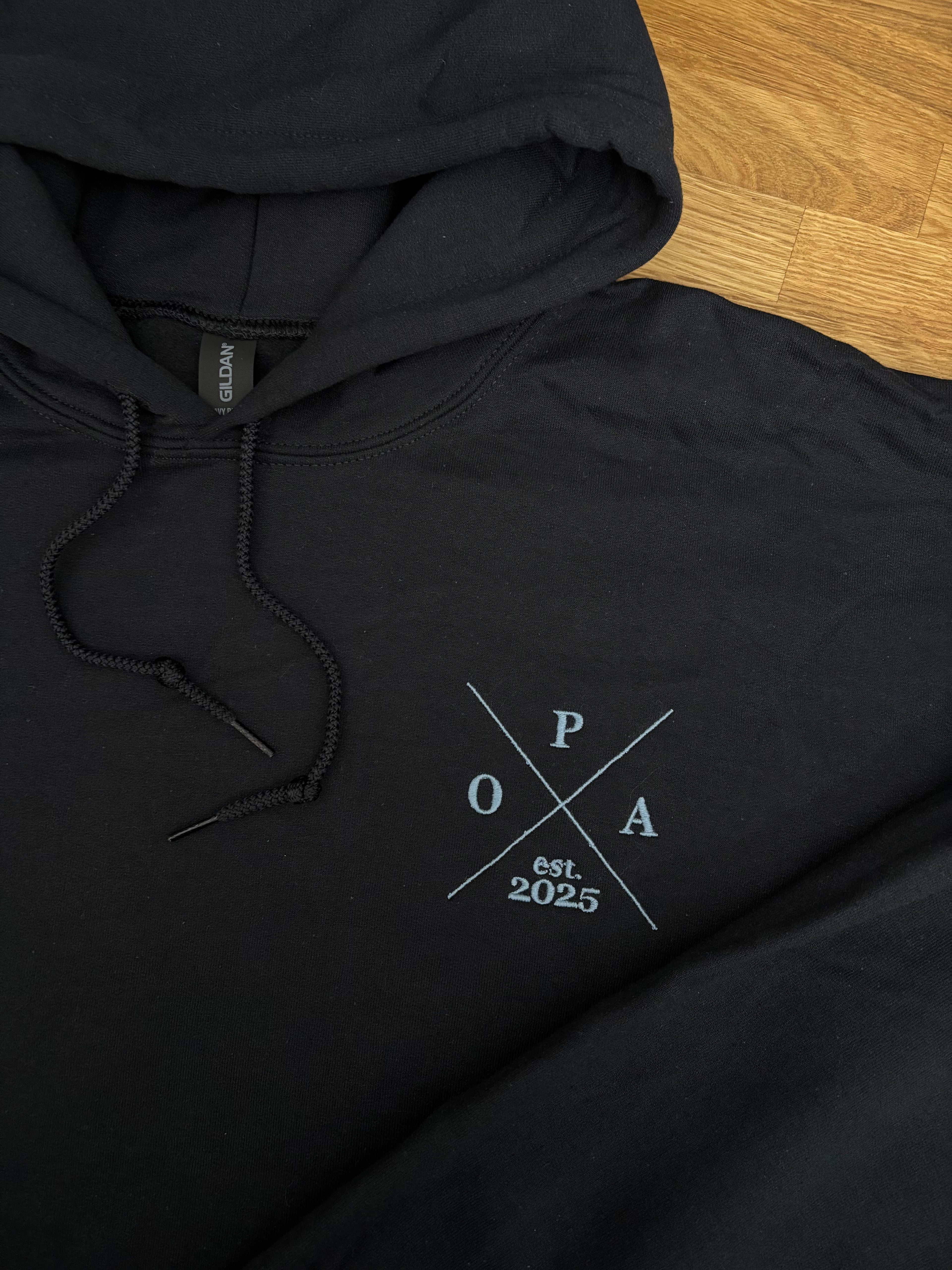 Ein Hoodie in der Farbe Schwarz mit einem Koordinaten Kreuz auf der linken Brust gestickt. Im Kreuz steht Opa est. 2025.