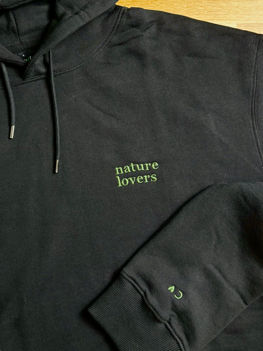 Der schwarze Pullover ist mit einem grünen Garn bestickt. Auf dem Pullover steht nature Kobers und auf dem Ärmel die Initalien C.