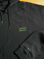 Der schwarze Pullover ist mit einem grünen Garn bestickt. Auf dem Pullover steht nature Kobers und auf dem Ärmel die Initalien C.