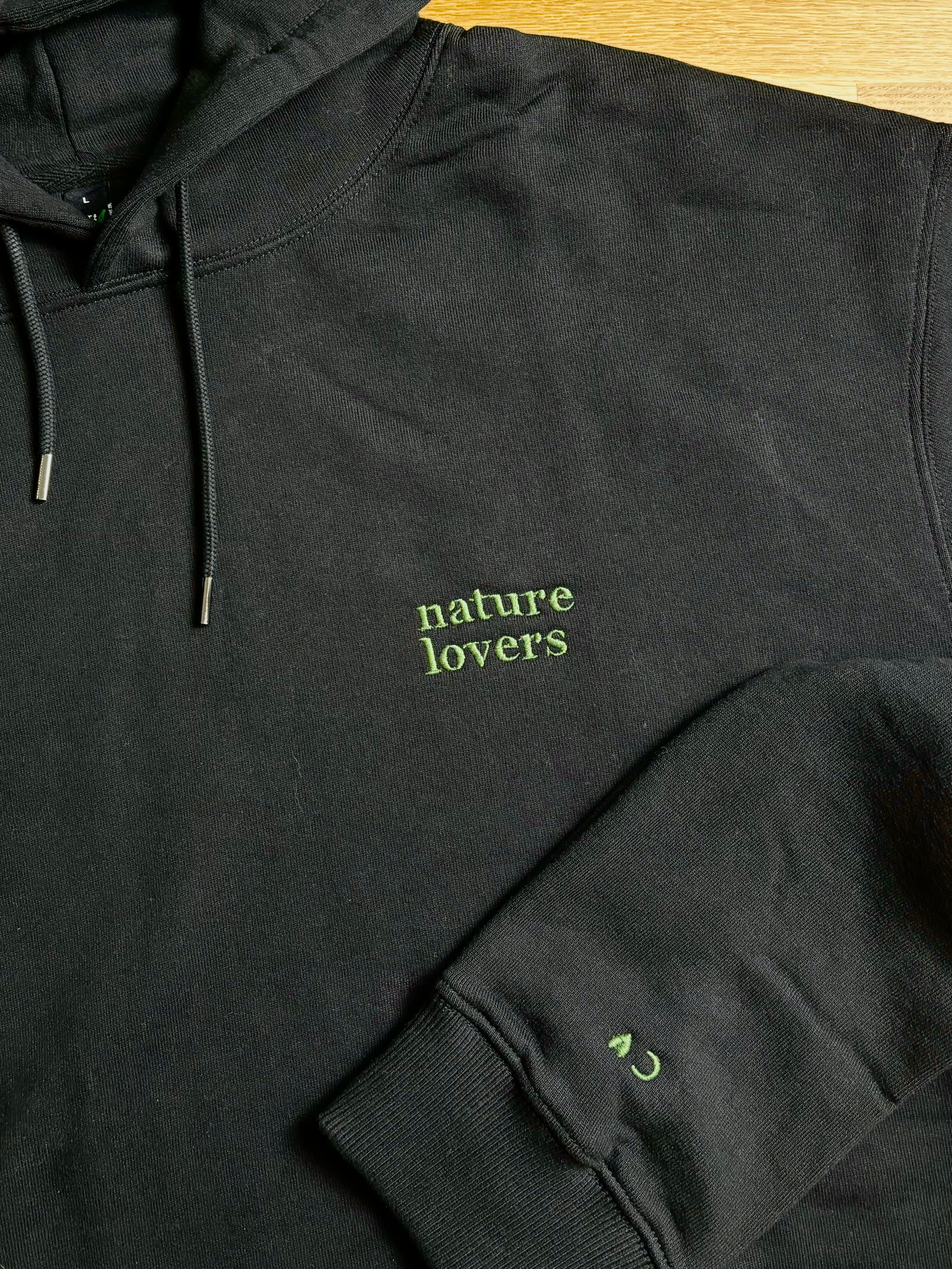 Der schwarze Pullover ist mit einem grünen Garn bestickt. Auf dem Pullover steht nature Kobers und auf dem Ärmel die Initalien C.