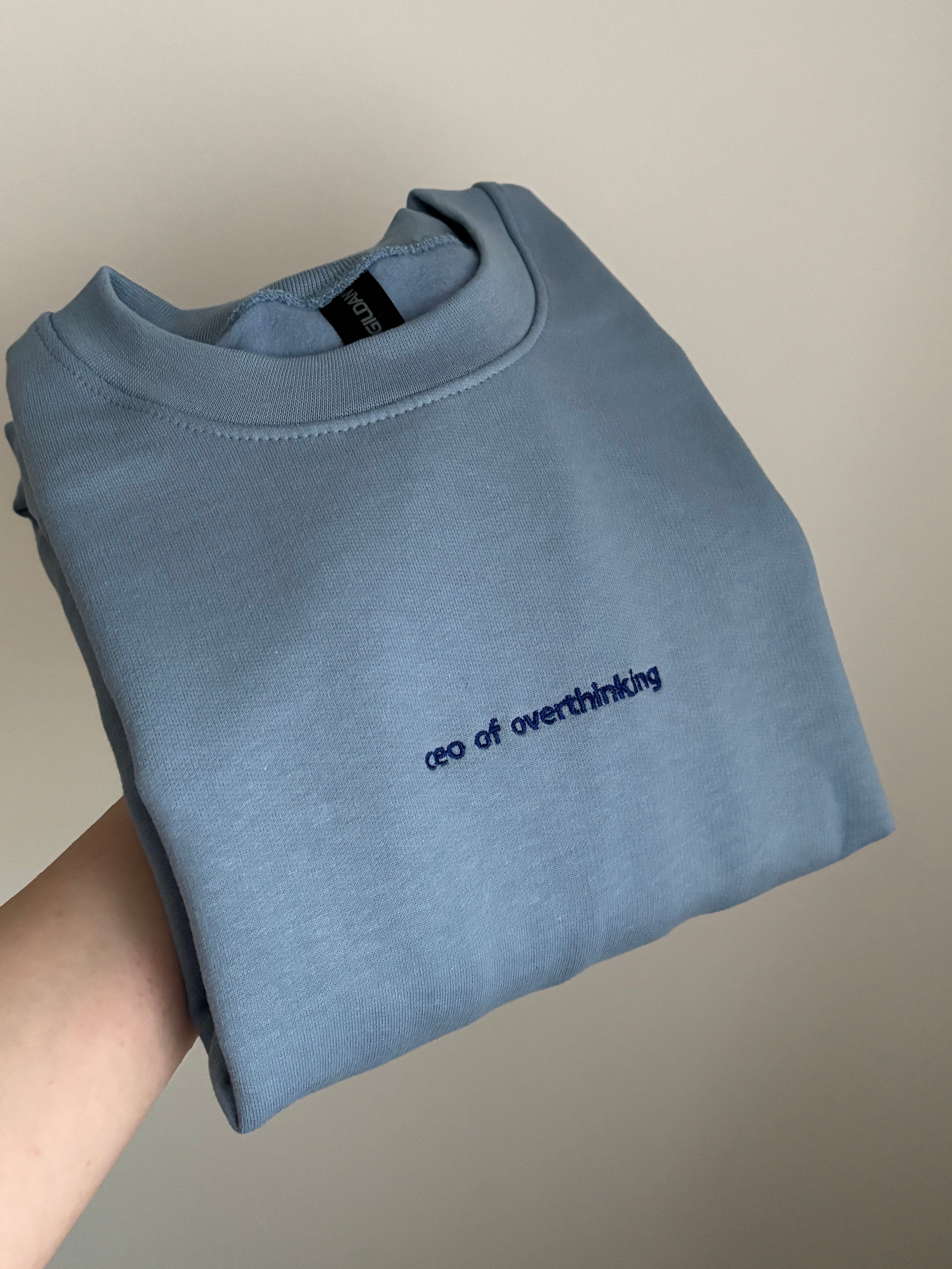 Ein Sweater in der Farbe Stone Blue mit einer Stickerei vorne mittig "ceo of overhinking" in Navy Blue.