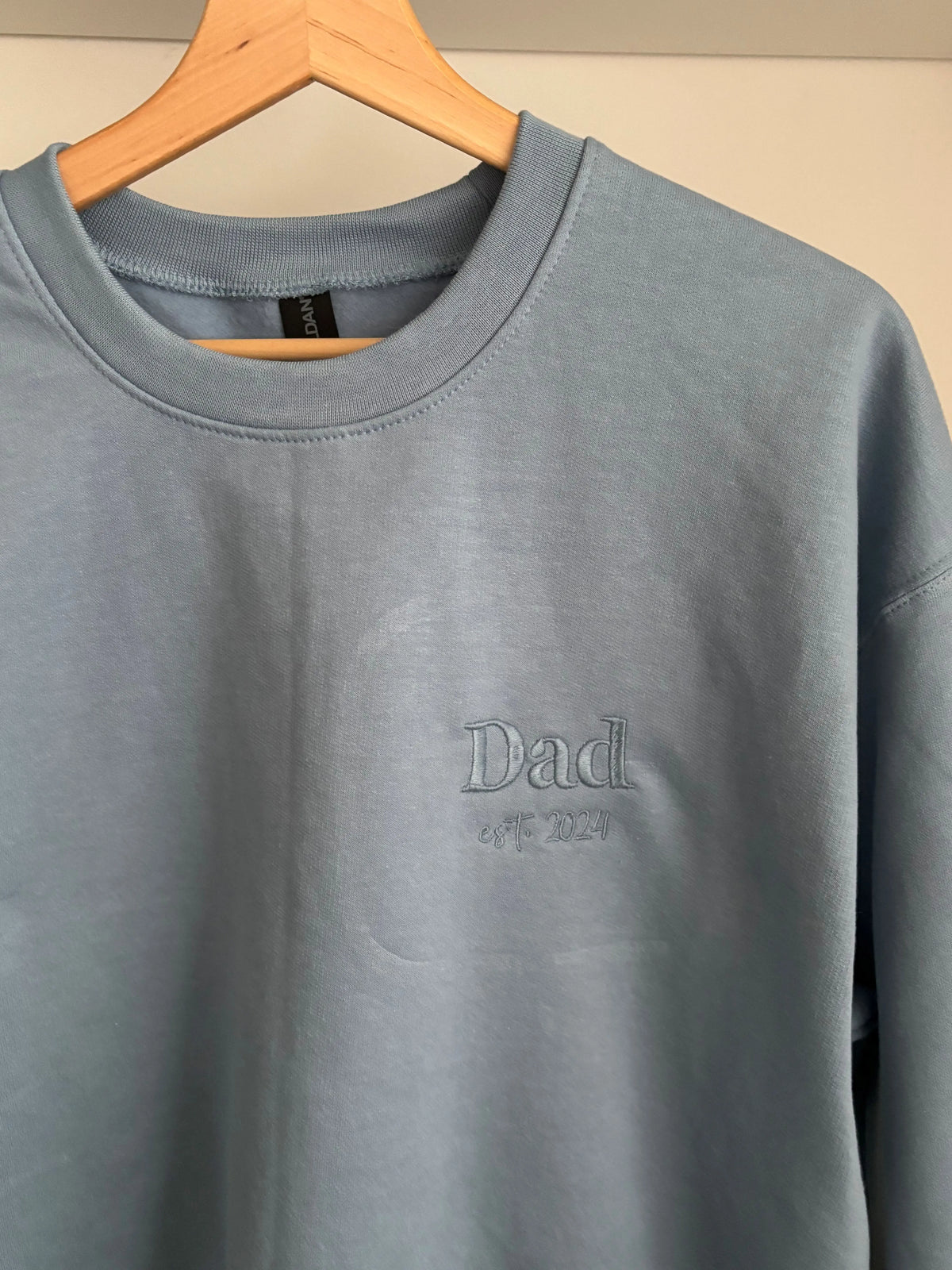 Ein Sweater in der Farbe Stone Blue mit einer Stickerei in der Farbe Stone Blue: Dad est. 2024.