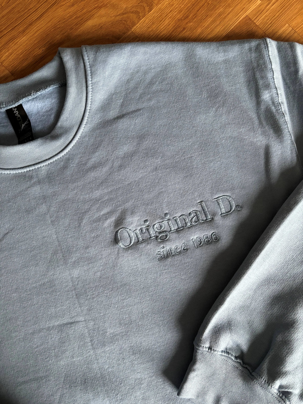Ein Sweater in der Farbe Stone Blue mit einer Stickerei auf der linken Brustseite: Original D. since 1986.