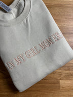 Ein Sweater in der Farbe Beige mit einem personalisierten Stick vorne auf der Brust mittig in poudre "In my girl mom era".