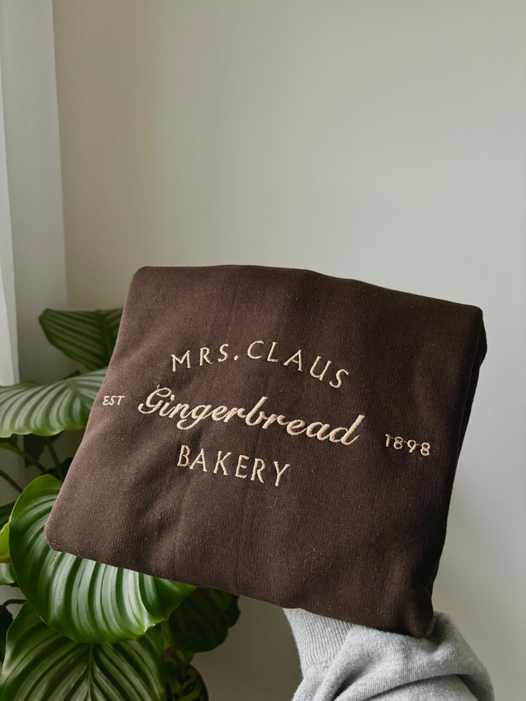 Ein kuschelig weicher Sweater für die kalte Jahreszeit. Bestickt mit Mrs. Claus Gingerbread Bakery in einem Karamell Ton.