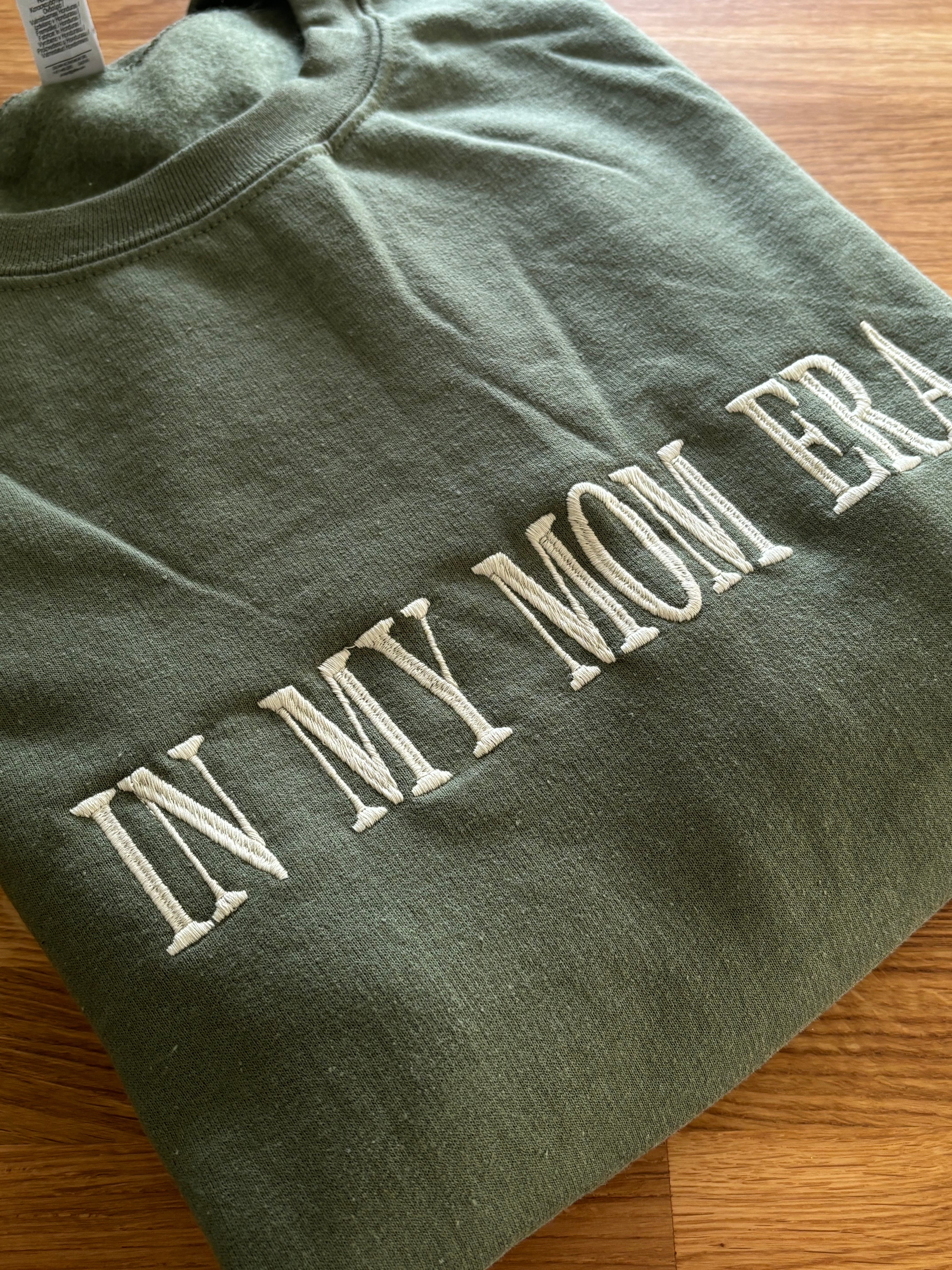 Ein Sweater in der Farbe Military Green mit einem bestickten Wunschtext vorne auf der Brust mittig in weiß "In my mom era".