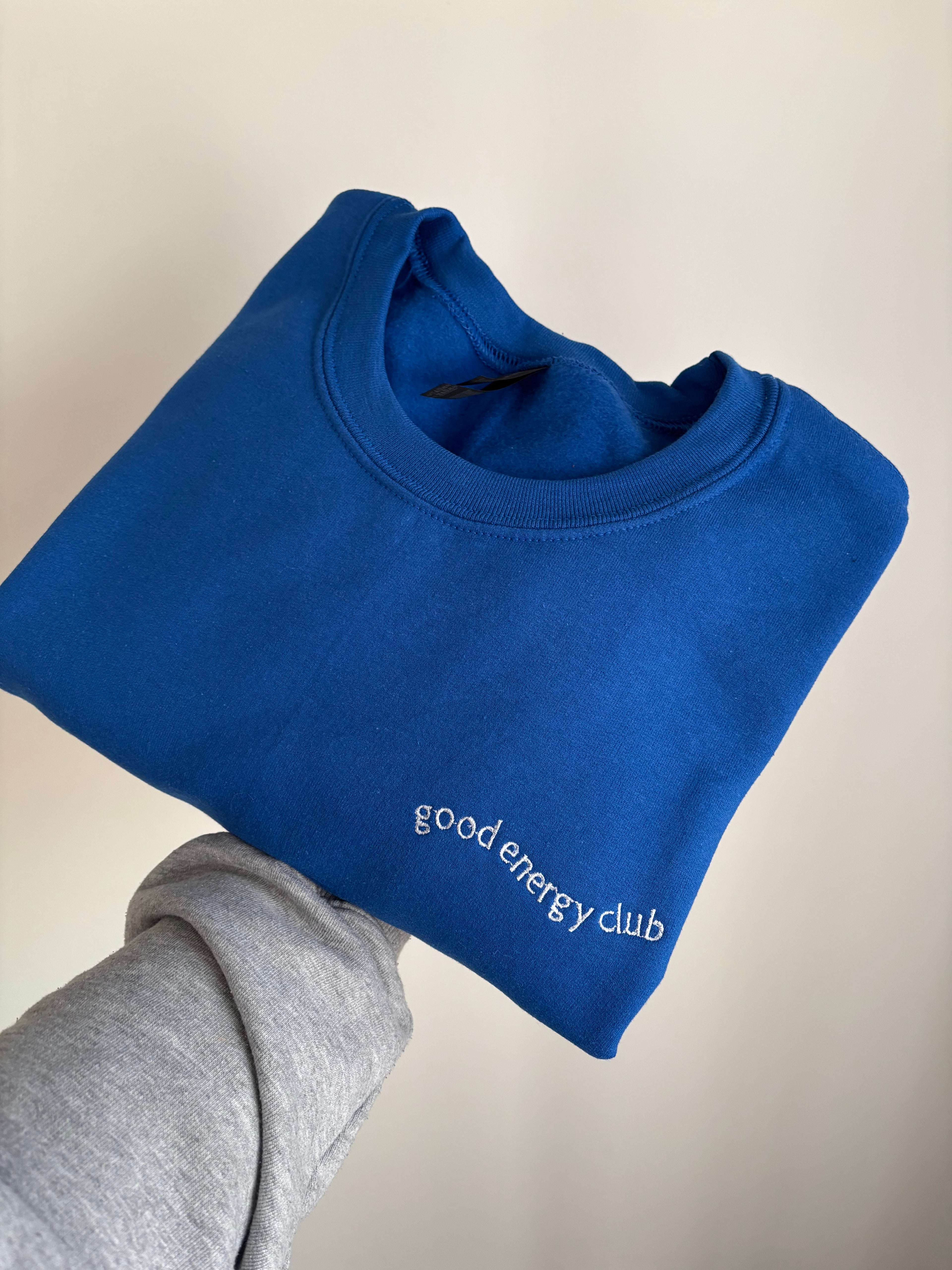 Ein Sweater in der Farbe Royal Blue mit einer Stickerek in weiß links: good Energy Club.