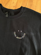 Der Cool Moms Club Sweater ist hier in schwarz mit buntem Garn bestickt. Der Stick sieht aus wie ein Smiley.