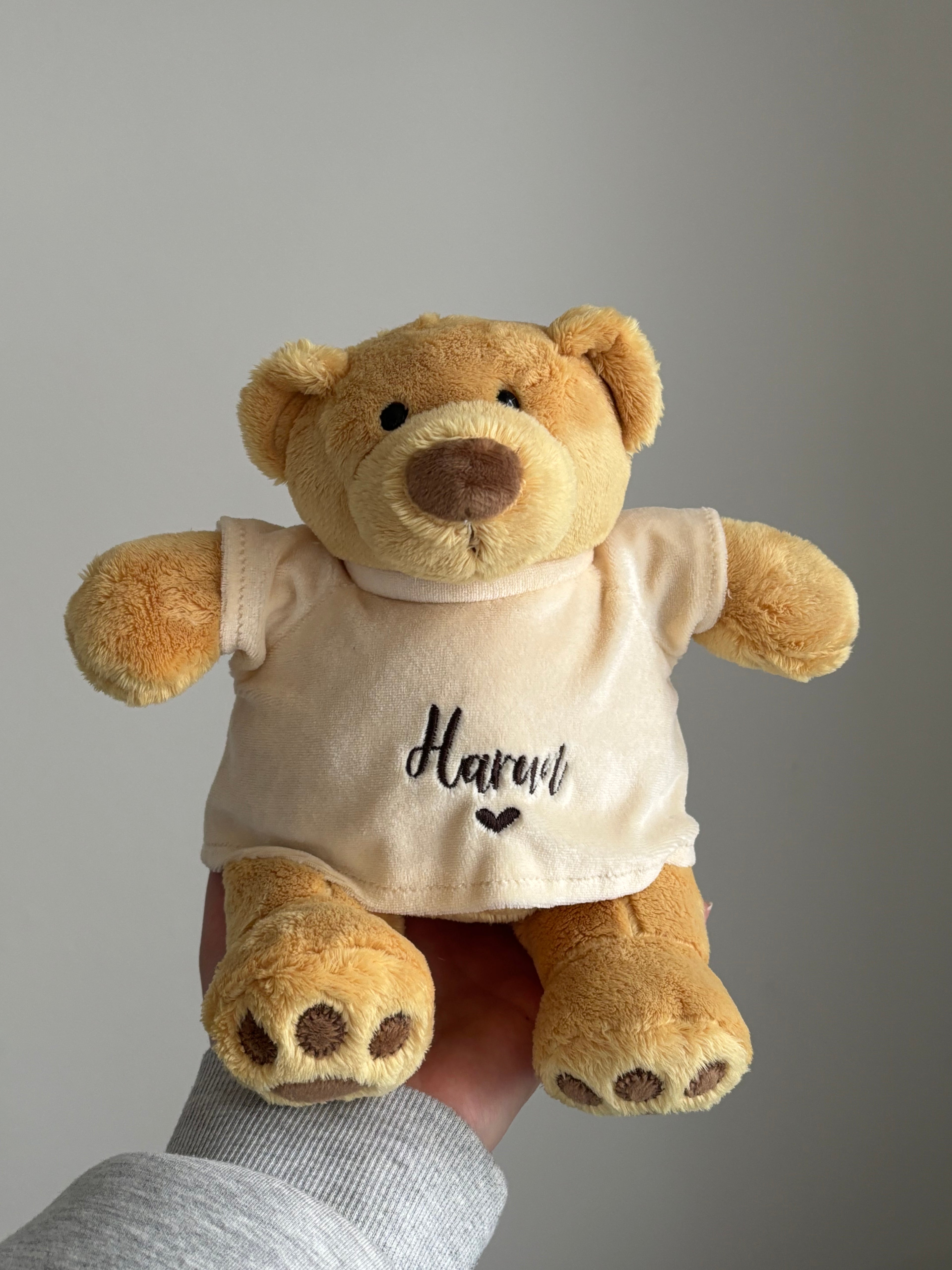 Brauner Teddybär mit einem T-Shirt. Vorne auf dem Shirt ist in dunkel braun Harun mit einem Herz gestickt.