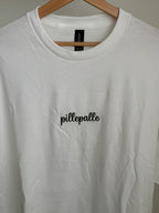 Ein T-Shirt in der Farbe Weiß mit einer dunkelgrünen Stickerei vorne mittig auf der Brust "pillepalle".