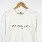 Ein weißer personalisierter Sweater mit einer Stickerei vorne Mama est 2024.