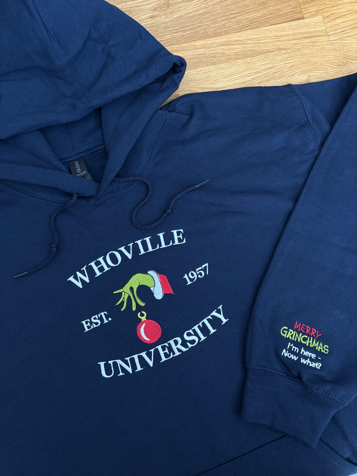 Der Whoville University Grinch Pullover in der Farbe Navy Blue. Auf dem Ärmel ist noch ein Grinch Spruch gestickt: Merry Grinchmas I‘m here - Now what?