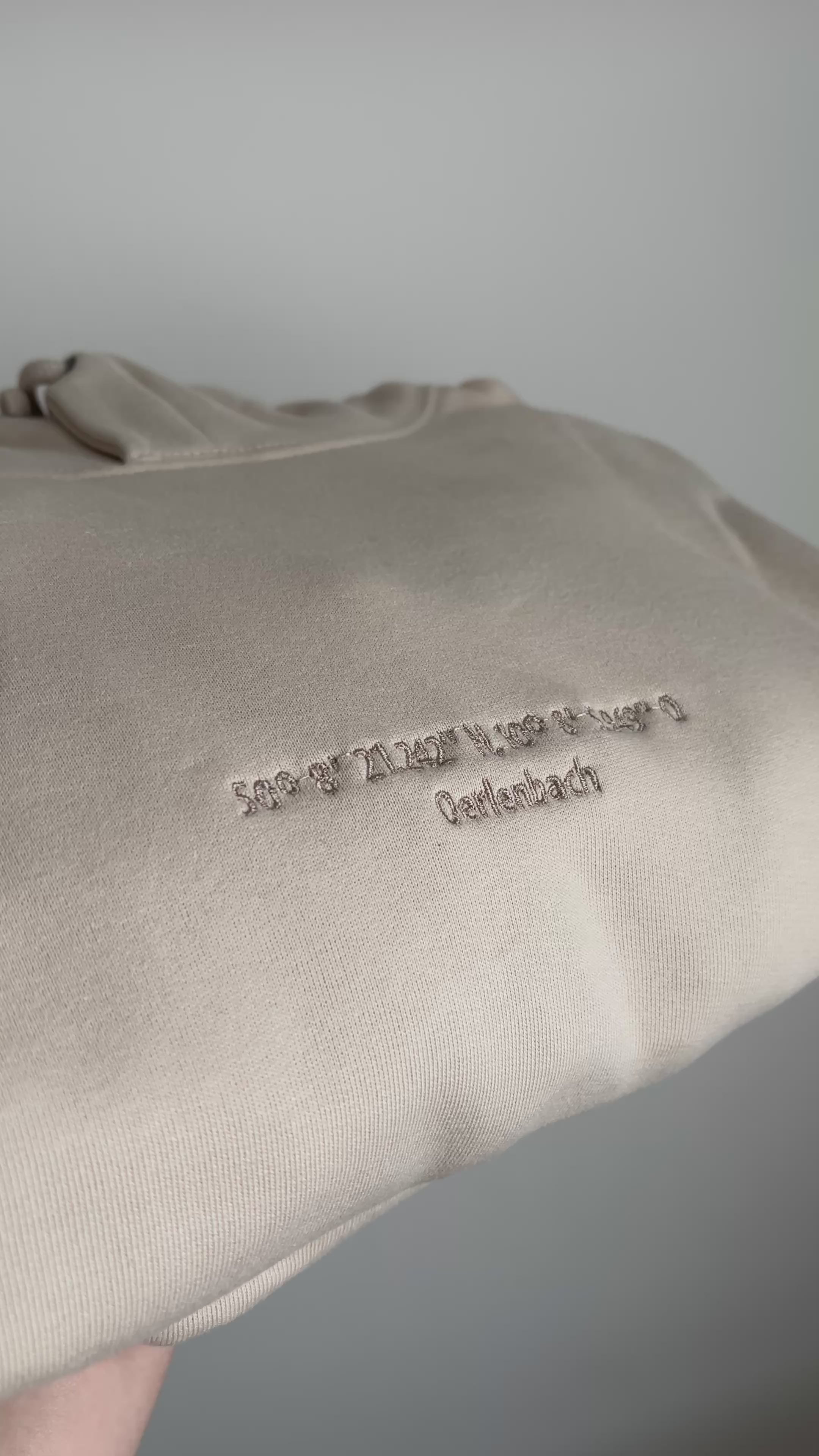 Ein beiger bestickter Hoodie mit Koordinaten und der Stadt in dunkelbeige.