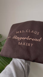 Ein kuschelig weicher Sweater für die kalte Jahreszeit. Bestickt mit Mrs. Claus Gingerbread Bakery in einem Karamell Ton.