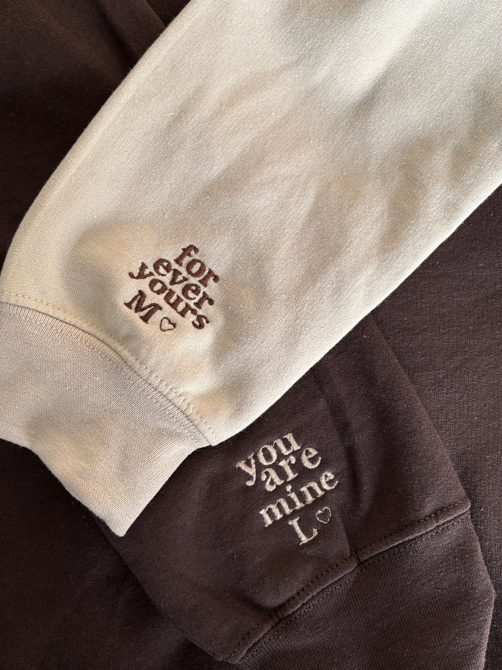 Zwei Ärmel in beige und dark chocolate liegen aufeinander. Auf dem beigen Hoodie ist in braun "for ever yours M" und auf dem dunkelbraunem in beige "you are mine L" gestickt.